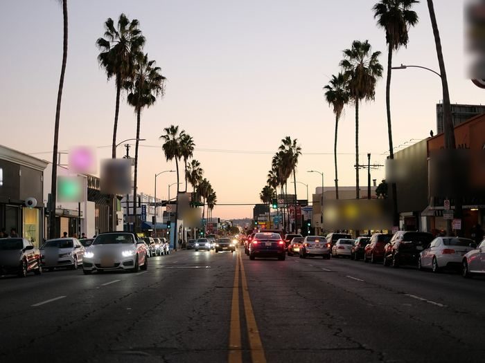 A palm-lined Los Angeles street at dusk, with traffic and evening lights