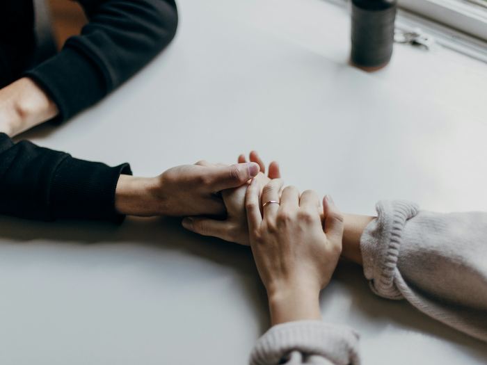 Two people holding hands across a table in a quiet gesture of support