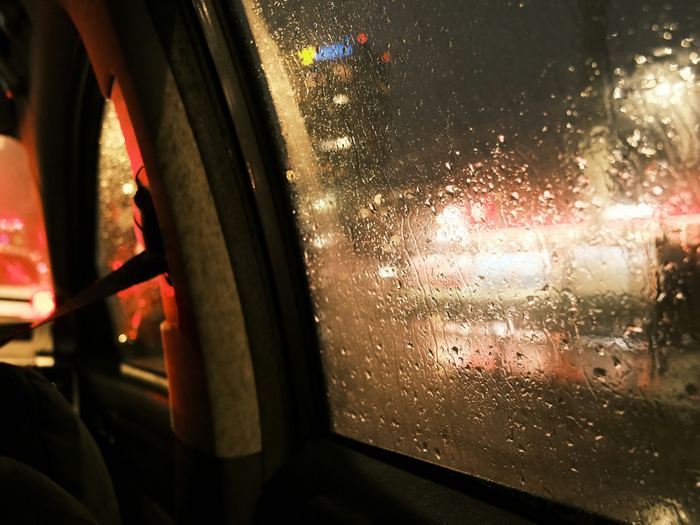 View from the back seat of a car on a rainy night, raindrops on the window and blurred city lights outside